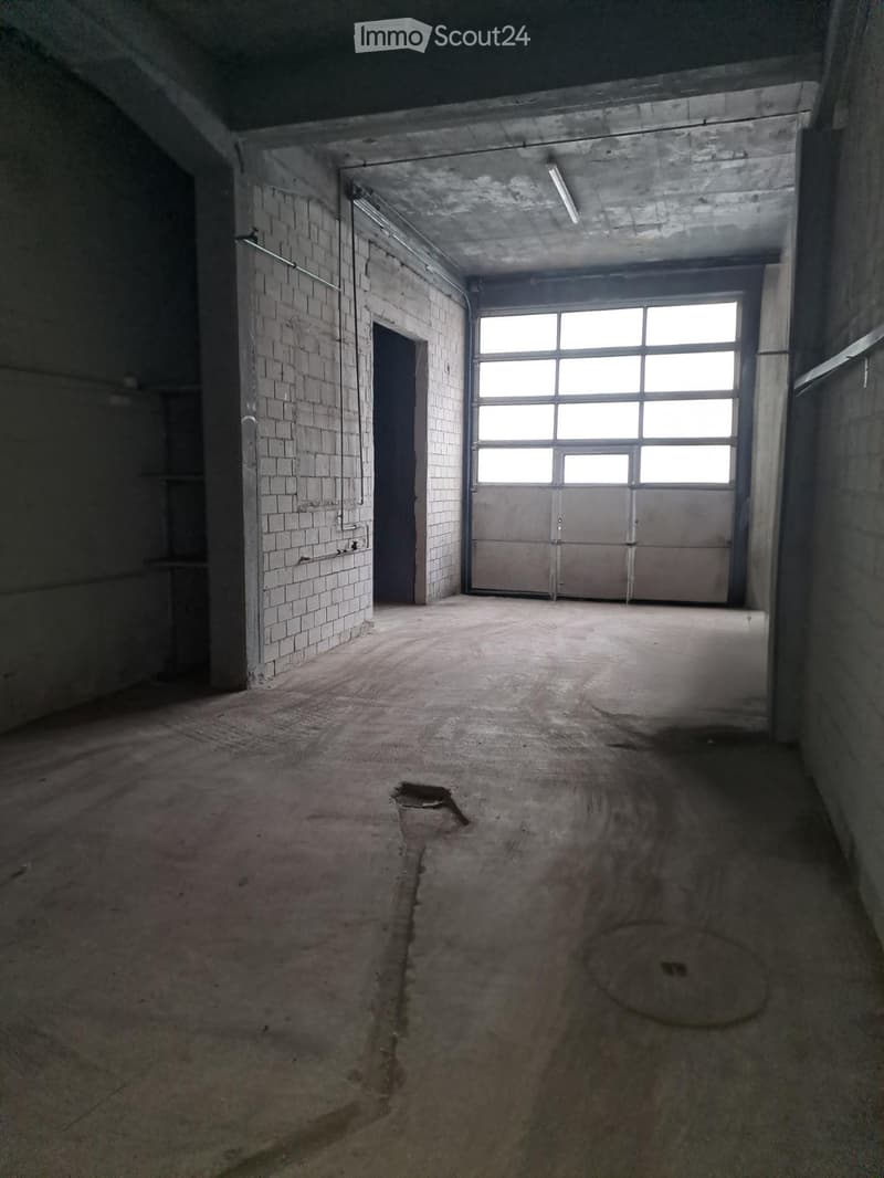 Empty room with exposed brick walls, concrete floor, and large garage-style door with windows. No furniture or equipment present.
