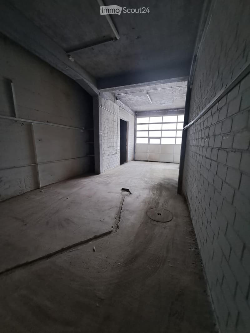 Empty industrial-style room with concrete floors, brick walls, and a large garage door at the far end.