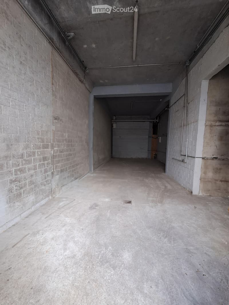 Empty concrete corridor with brick walls, leading to a garage area.