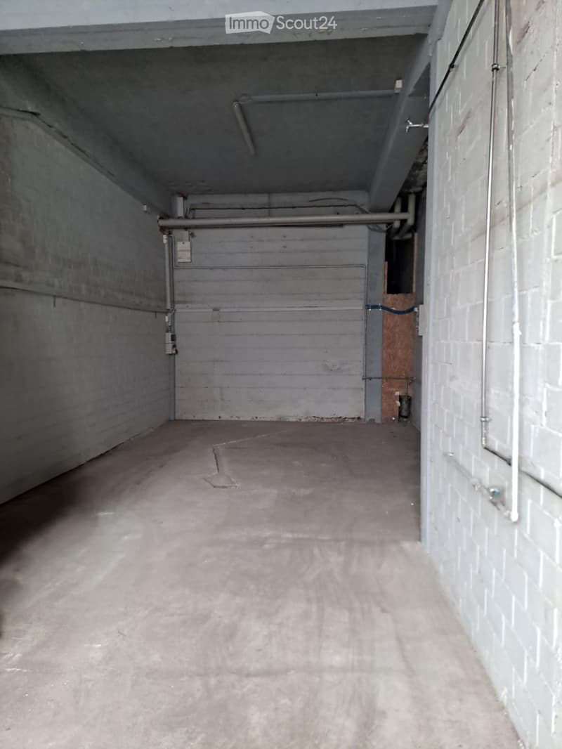 Empty garage with concrete floor, brick walls, and a large metal door. No furniture or equipment present.