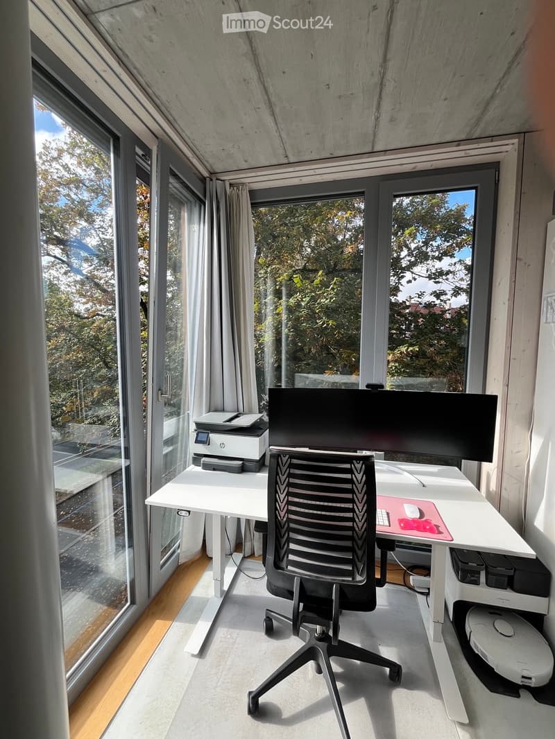 Modern, minimalist office space with large windows, a white desk, ergonomic chair, printer, and computer screen.