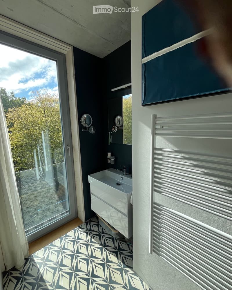 Modern bathroom with dark walls, white sink, geometric patterned floor, large window with view, and radiator.