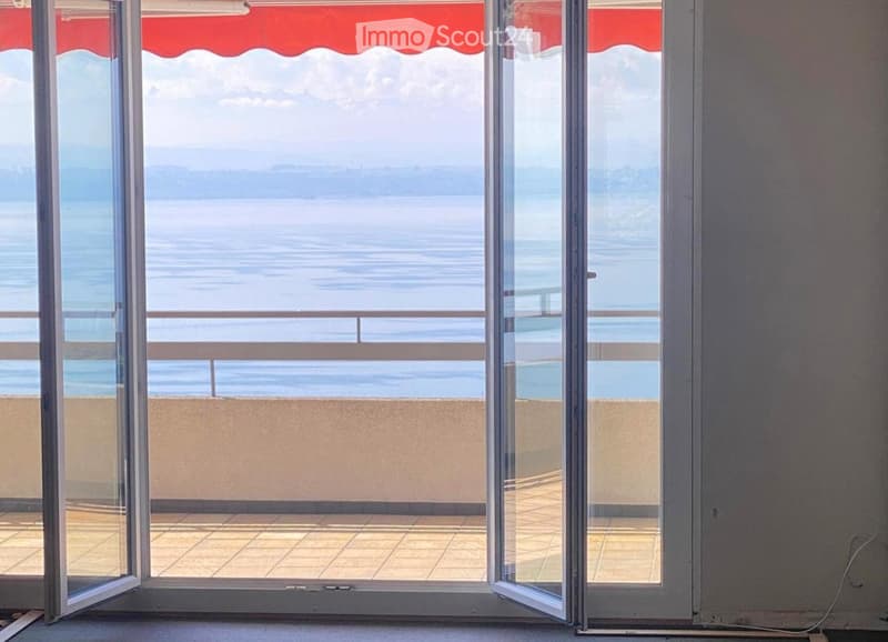 Open sliding glass doors leading to a balcony with a view of the sea and distant hills.