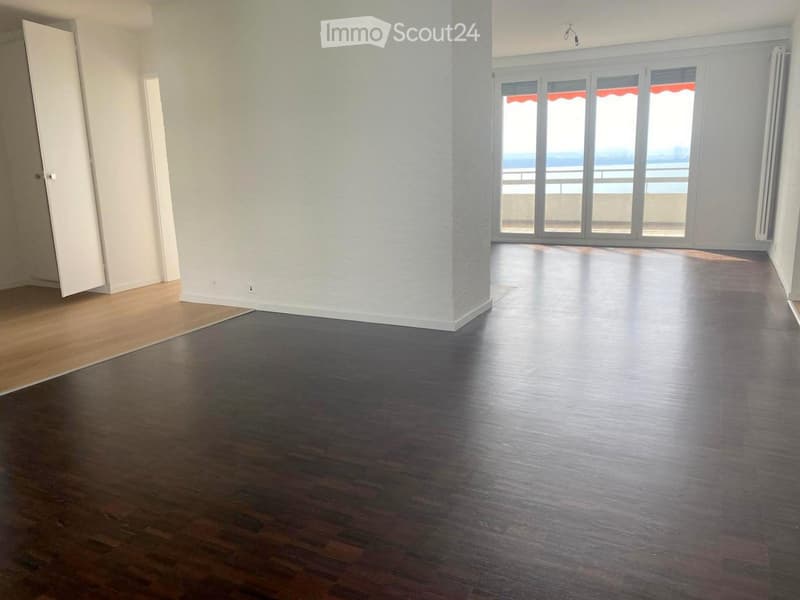 Empty room with dark wooden flooring, white walls, and large glass doors leading to a balcony with a view of the sea.