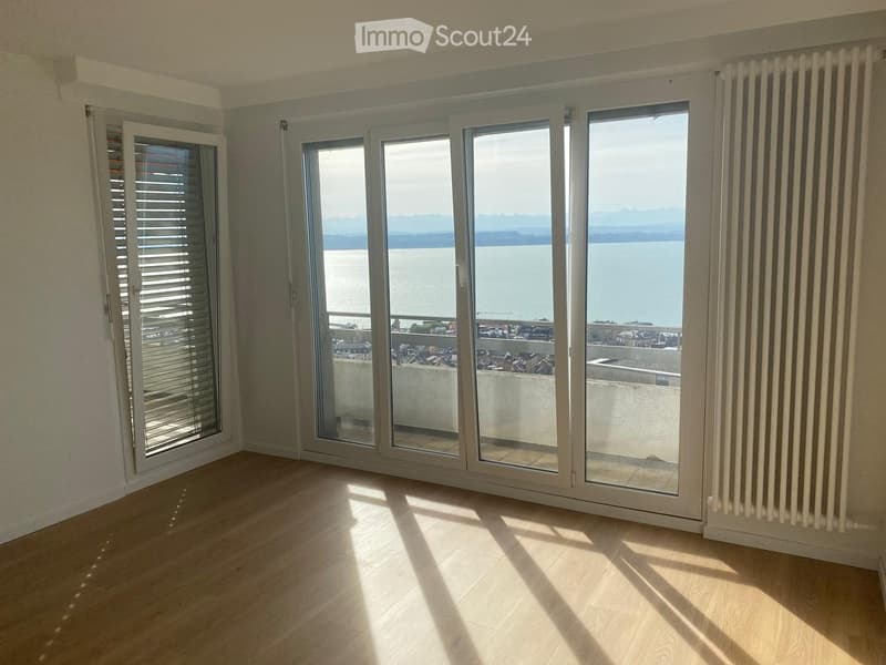 Empty room with wooden flooring, large windows offering a scenic view of the water and distant landscape.