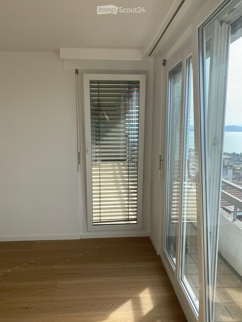 Empty room with wooden flooring, large windows, and a view of the lake and surrounding area.