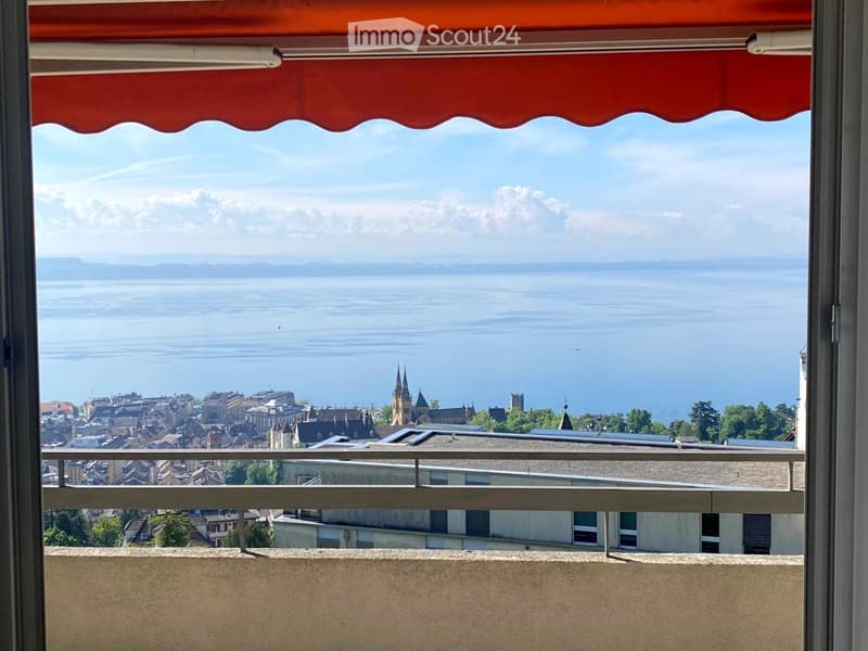 Balcony with a view of a lake and town, featuring a red awning and metal railing.