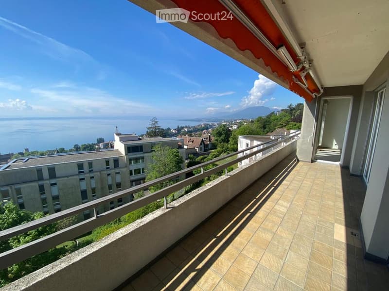 Balcony with tiled floor, metal railing, and a view of a lake and distant mountains.