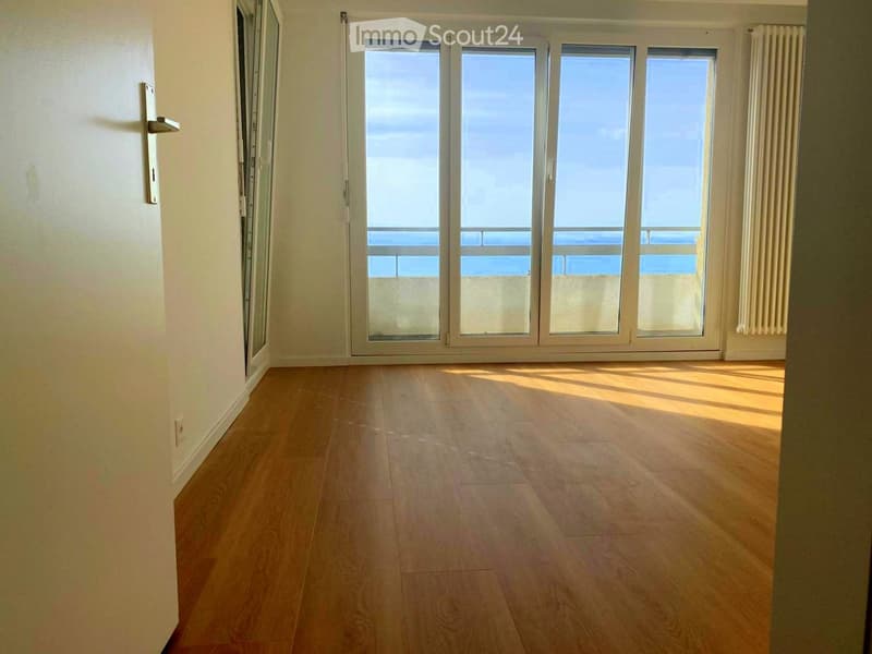 Empty room with wooden flooring, large glass sliding doors leading to a balcony, and natural light streaming in.