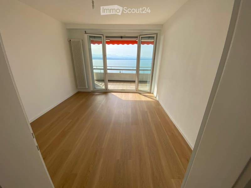 Empty room with wooden flooring, white walls, and large sliding glass doors leading to a balcony with a sea view.