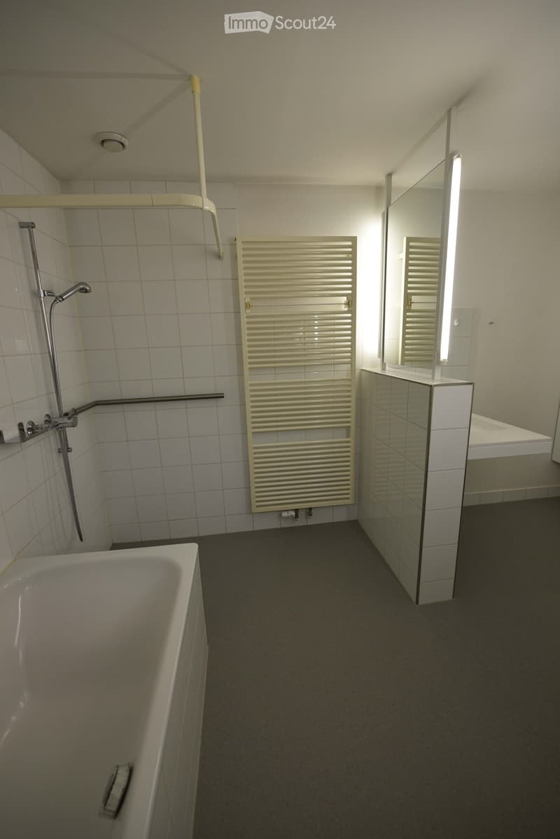 Modern bathroom with a bathtub, shower, mirror, and radiator. The space features tiled walls and a dark grey floor.