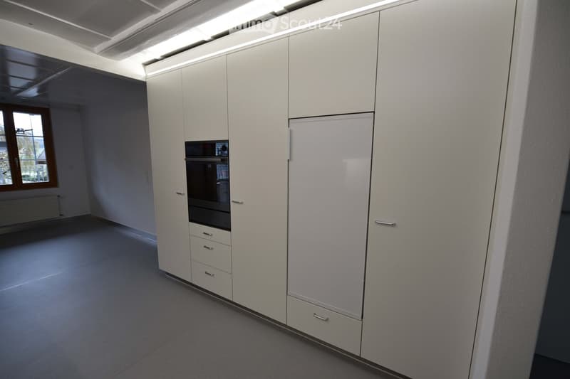 Empty kitchen area with white cabinets, a built-in oven, and a window with a view of the outside. The space is clean and unfurnished.