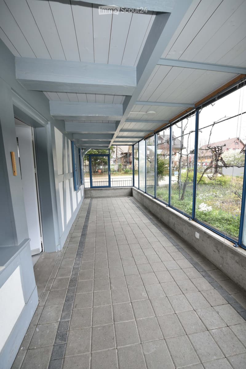 Empty balcony with tiled floor, large windows, and a view of the surrounding area.