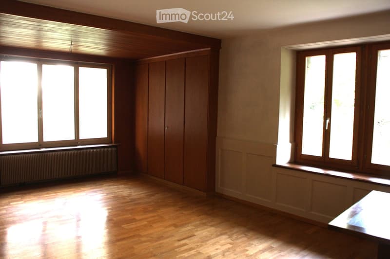 Empty room with wooden flooring, large windows, and built-in wooden cabinetry. No furniture or personal items present.
