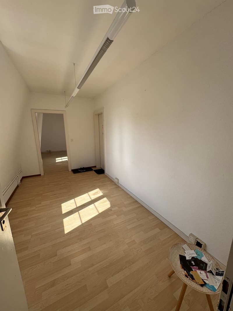 A small, unfurnished hallway with wooden flooring, white walls, and a small round table holding brochures.