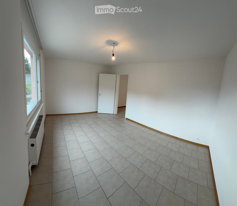 Empty room with tiled floor, white walls, large window, and a single door leading to another space.