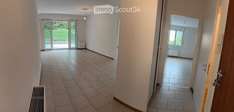 Empty hallway with tiled flooring, white walls, and a sliding glass door leading to an outdoor area. A radiator is visible on the left side.