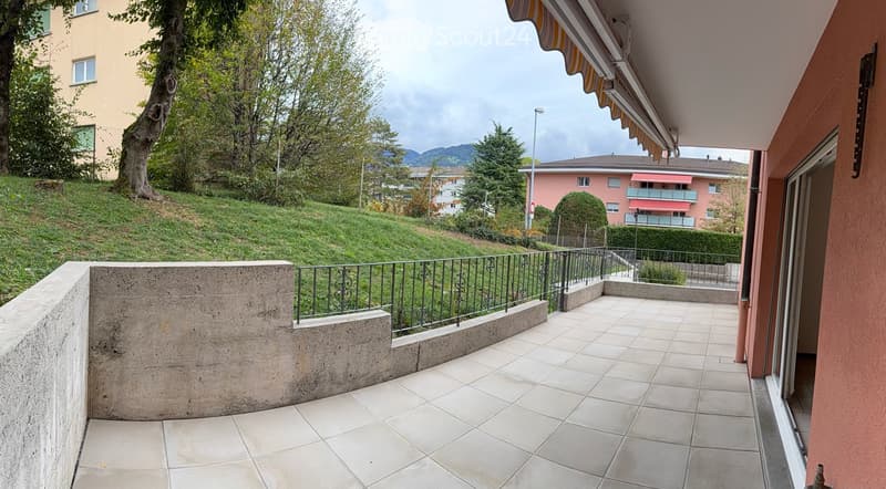 Balcony with tiled floor, metal railing, and view of a green hillside and neighboring buildings.