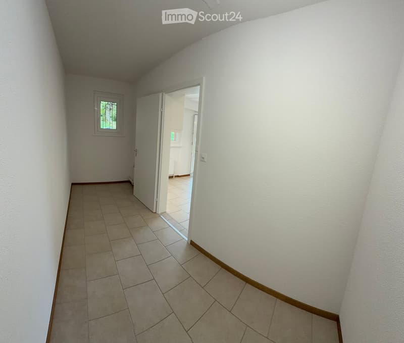 Empty hallway with tiled floor, white walls, and an open door leading to another room.