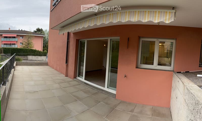 Balcony with tiled floor, sliding glass doors leading to interior, striped awning above, metal railing, and view of neighboring building.