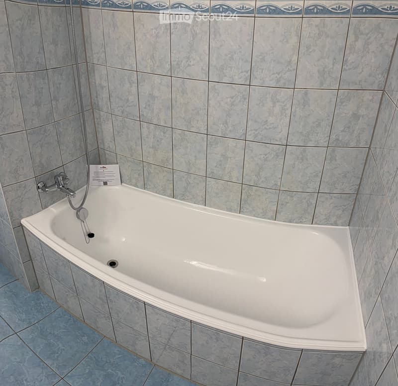 Modern bathroom with a white bathtub, grey tiled walls, and a chrome faucet.