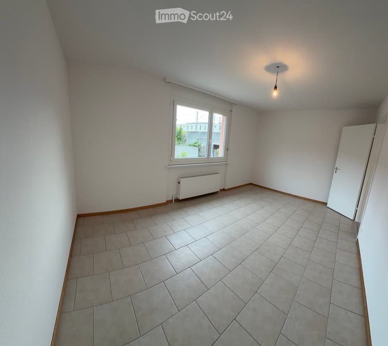 Empty room with tiled floor, white walls, a window with blinds, a radiator, and a single light fixture on the ceiling.