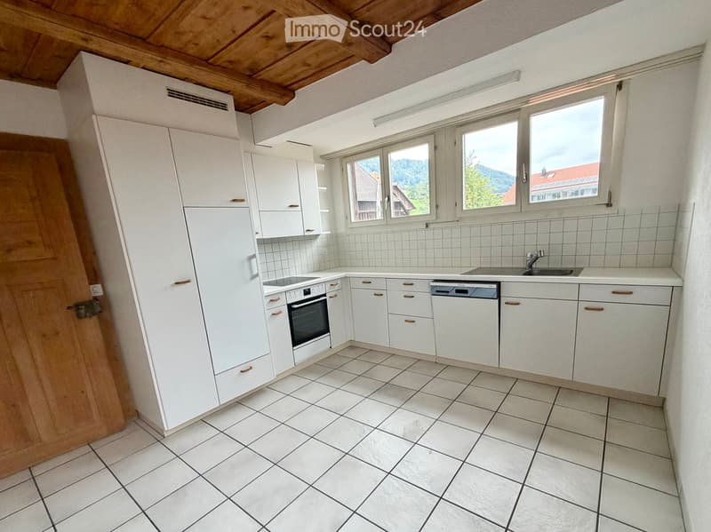 Bright kitchen with white cabinets, tiled floor, and large windows offering a scenic view.