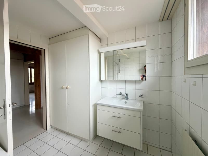 Modern bathroom with white tiled walls and floor, a white sink with a mirror above it, and a white cabinet with drawers.
