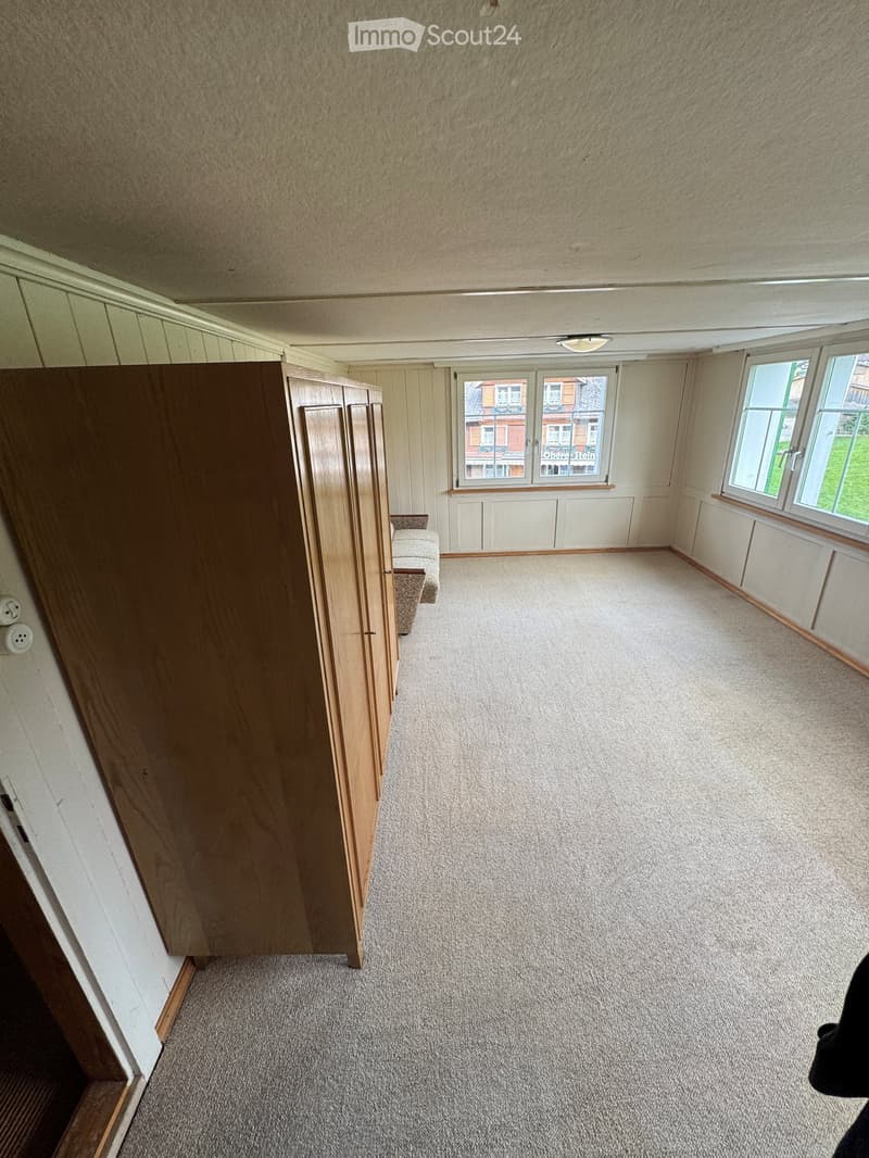 Empty room with carpeted floor, wooden wardrobe, and windows showing a view of the street.