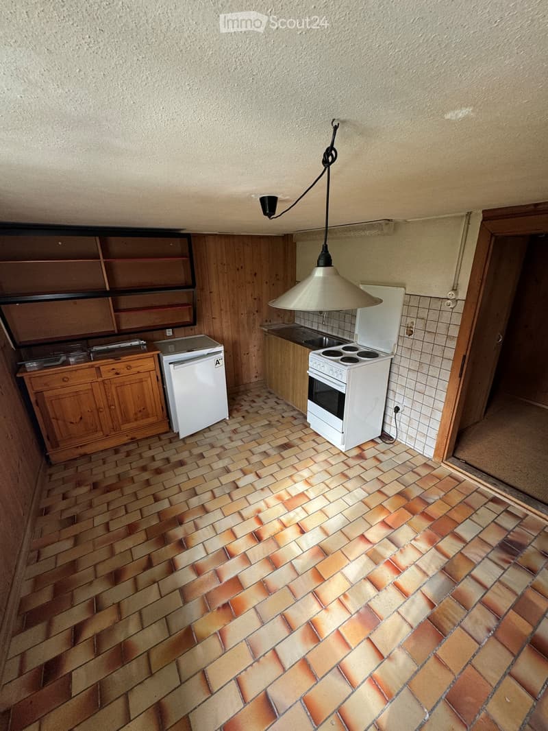 Small kitchen with tiled floor, wooden cabinets, white refrigerator, and electric oven. Features a pendant light hanging from the ceiling.