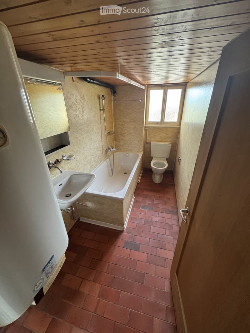 Bathroom with a bathtub, toilet, sink, and mirror, featuring wooden paneling on the ceiling and walls, and a tiled floor.