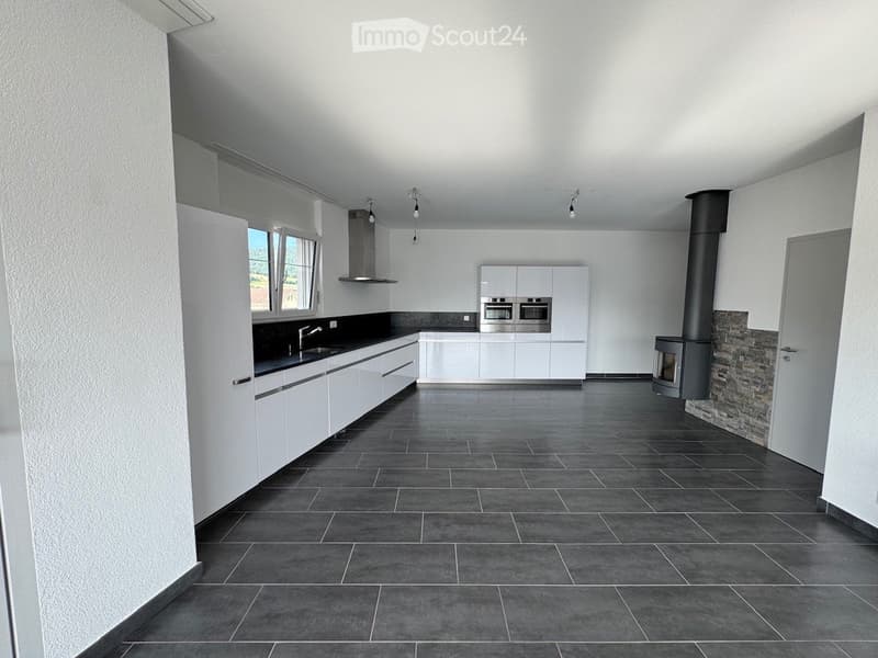 Modern kitchen with white cabinets, stainless steel appliances, dark countertops, and a tiled floor. Features a built-in oven, range hood, and a stone fireplace.