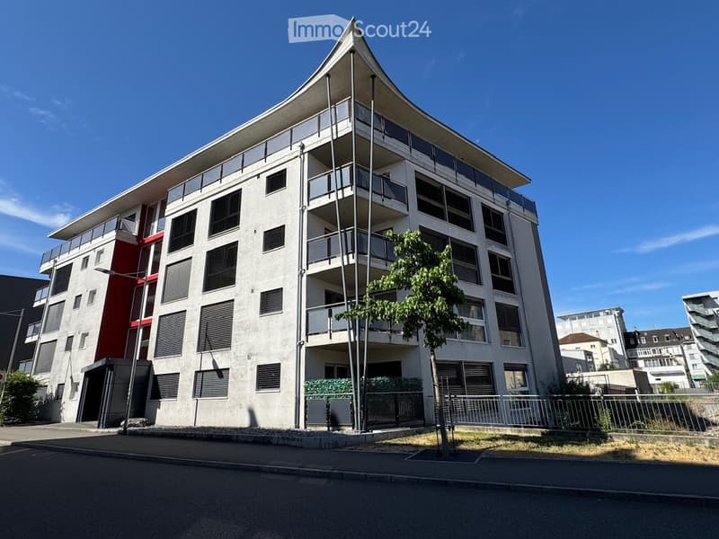 Modern multi-story residential building with balconies, large windows, and a distinctive angular roofline.