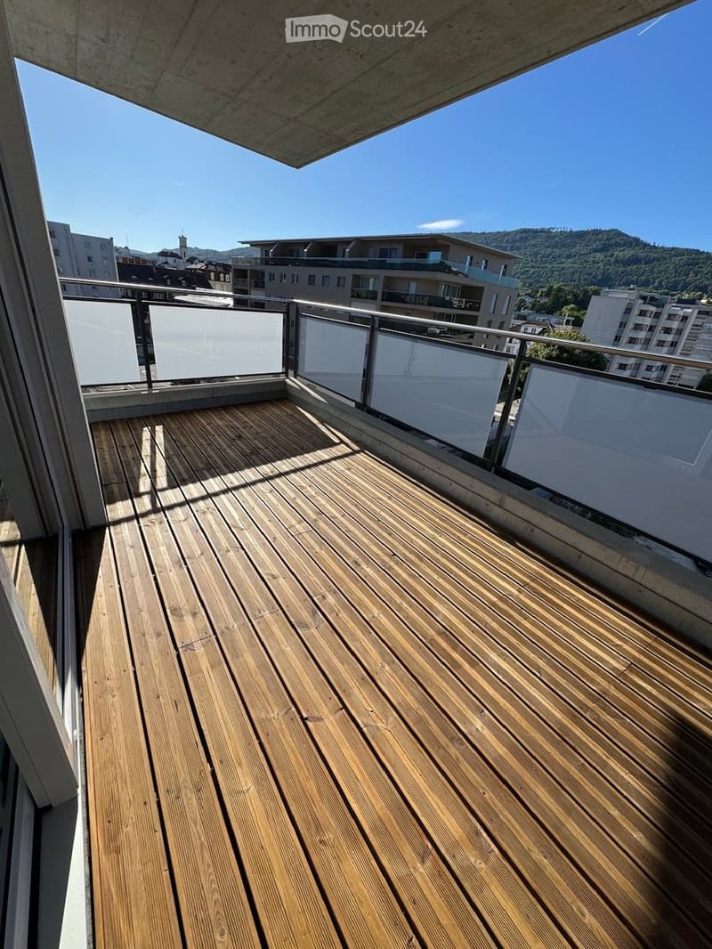 Wooden deck with glass balustrade, overlooking cityscape and mountains.
