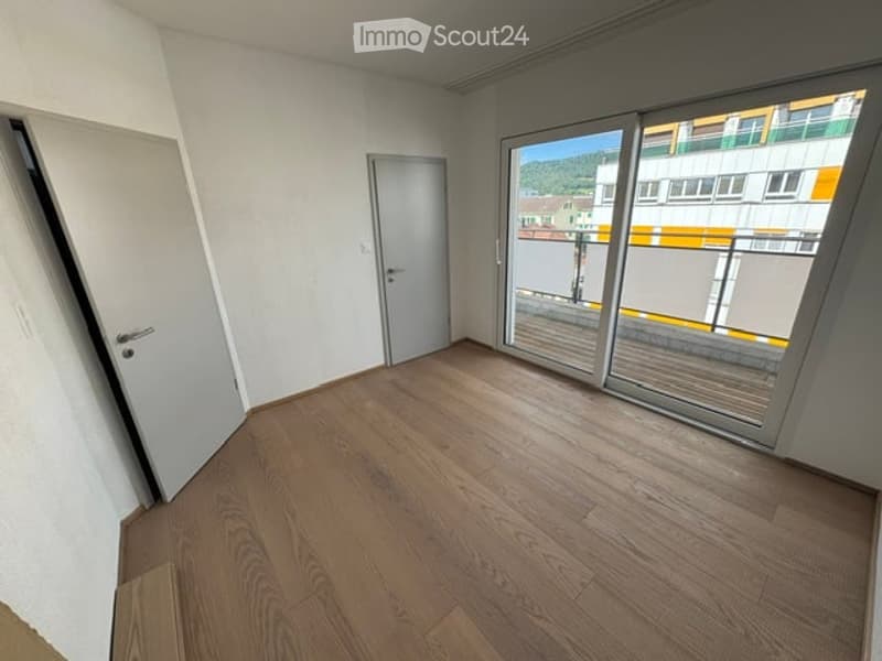 Empty room with wooden flooring, white walls, and large glass sliding doors leading to a balcony.