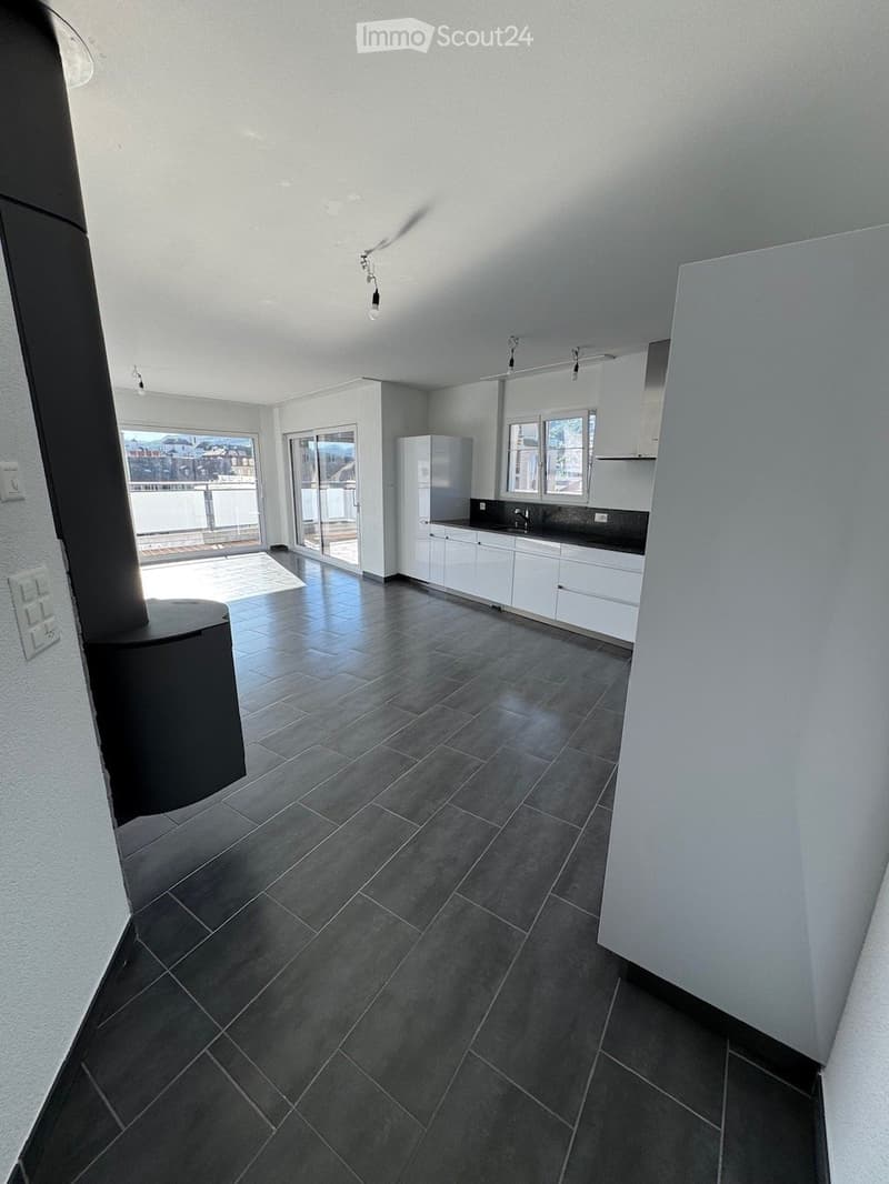 Modern kitchen with white cabinets, dark tiled floor, and a view of a balcony through large windows.