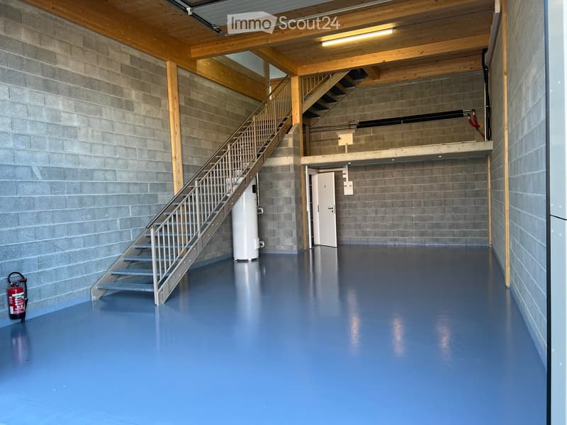 Empty hallway with blue epoxy floor, gray concrete walls, metal staircase leading to an upper level, white water heater, and a red fire extinguisher on the floor.