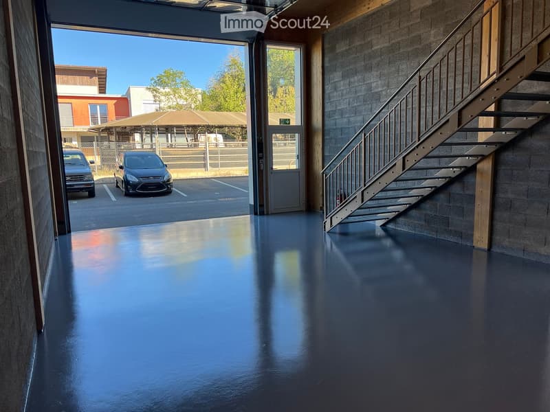 A modern, empty corridor with a polished dark blue floor, a metal staircase leading upwards, and an open doorway leading to a parking area with two parked cars.