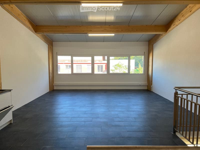 Empty room with dark tiled floor, white walls, large windows, and exposed wooden beams on the ceiling.