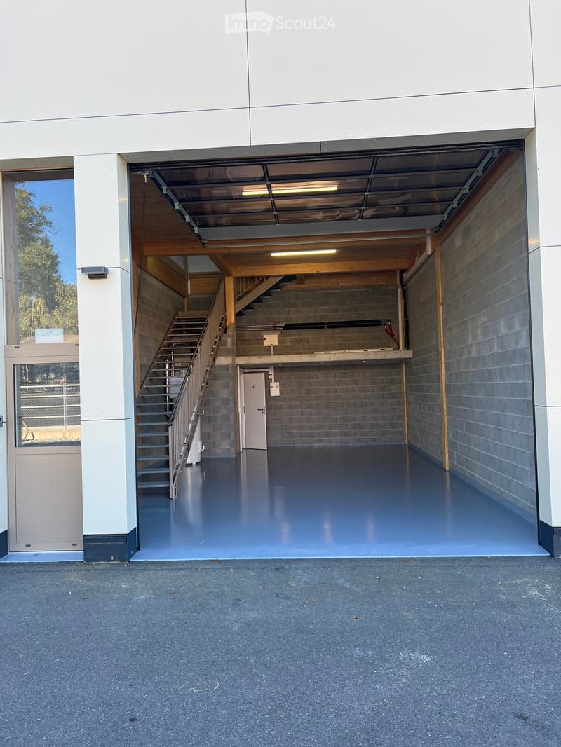 Modern garage with a staircase leading to an upper level, featuring a polished blue floor and wooden beams.
