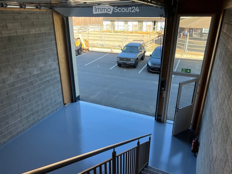 Hallway with blue flooring, metal railing, and access to a parking area with two parked cars.