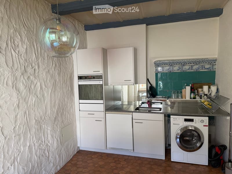 Modern kitchen with white cabinets, stainless steel appliances, and a tiled backsplash. Features an oven, dishwasher, washing machine, and sink.