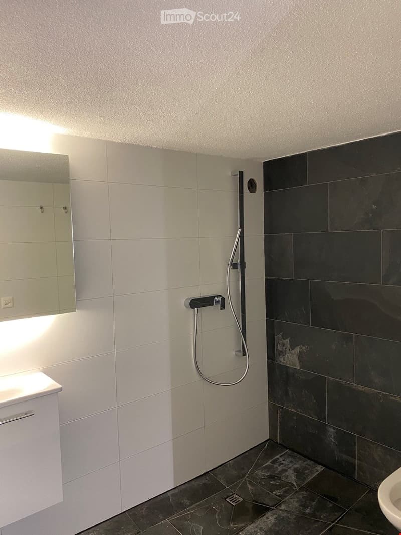 Modern bathroom with white tiled walls, black tiled shower area, a large mirror, and a sleek shower system.