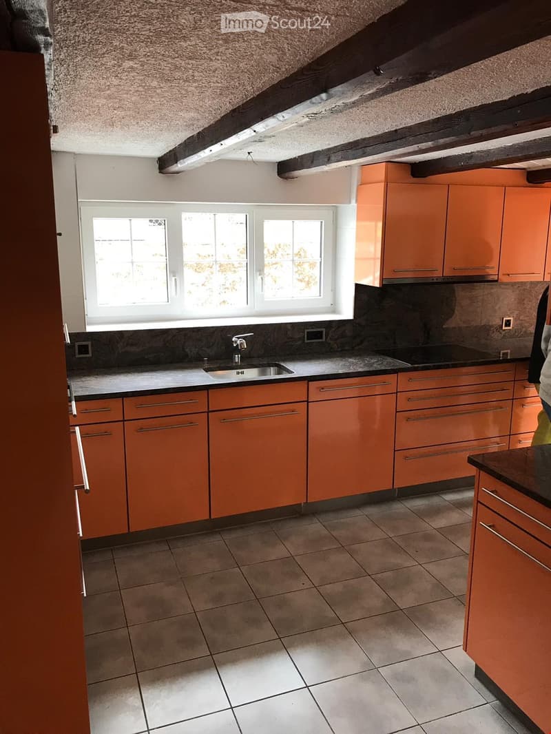Modern kitchen with orange cabinets, granite countertops, and a stainless steel sink.