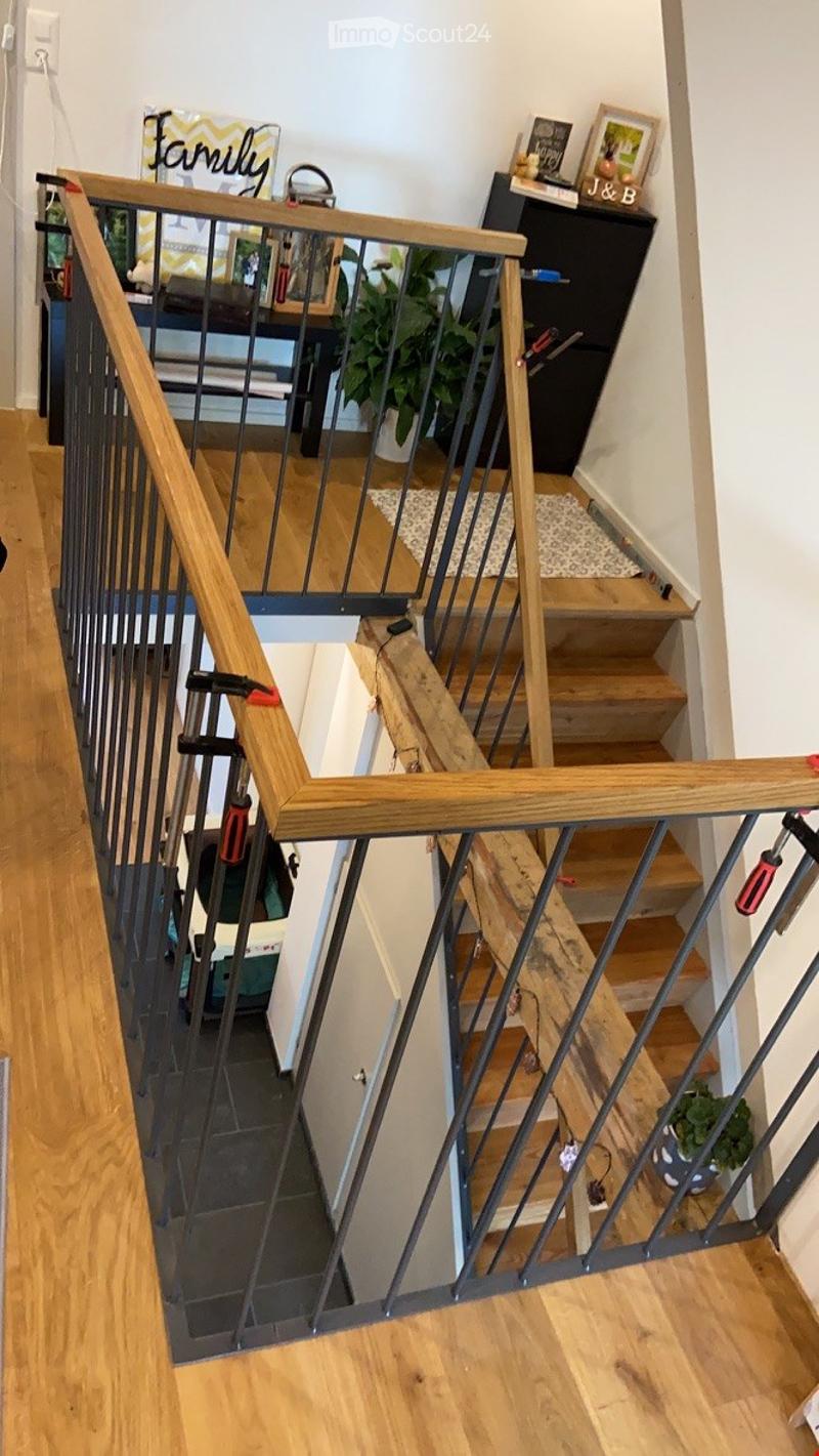 Staircase with wooden railings and steps, leading to an upper level. The lower level has a tiled floor, and the upper level has wooden flooring.