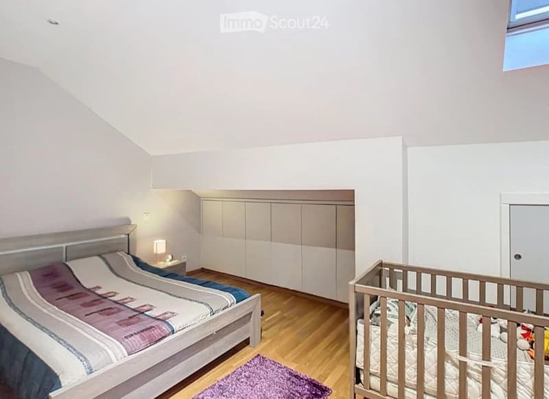 Bright bedroom with wooden flooring, a double bed with patterned bedding, a nightstand with a lamp, built-in wardrobes, and a crib with toys.