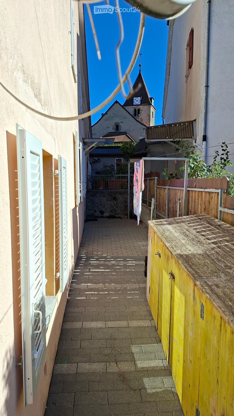 Narrow brick-paved alleyway between buildings, with wooden fence and small garden area visible at the end.