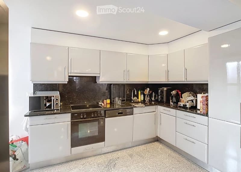 Modern kitchen with white cabinets, black countertops, and stainless steel appliances including a microwave, oven, dishwasher, and coffee maker.