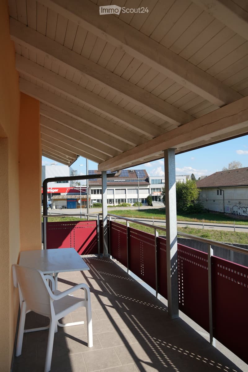 Balcony with a white table and chair, wooden ceiling, and red privacy screens.