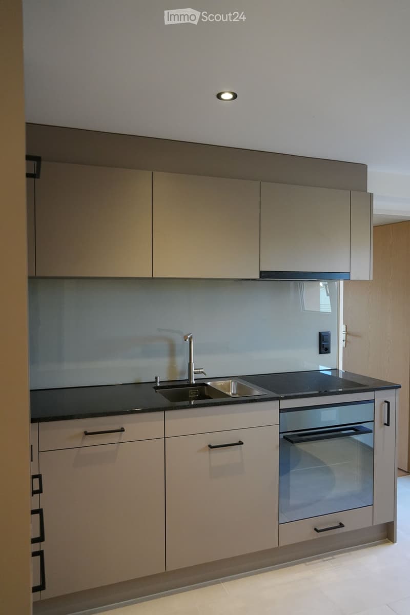 Modern kitchen with light-colored cabinets, a black countertop, a sink with a modern faucet, and an oven with a glass door.